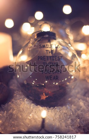Christmas and new year decoration - glass ornament with text "a smile is 
the prettiest thing you can wear", candle and christmas lights;  festive background 
