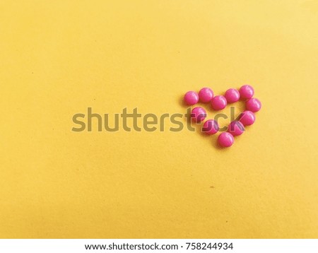 Heart shape of pink medicine pills on yellow background. Minimal style. Medical and healthcare concept.