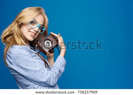 blonde in glasses is holding a retro camera on a minus background. empty space for copying.