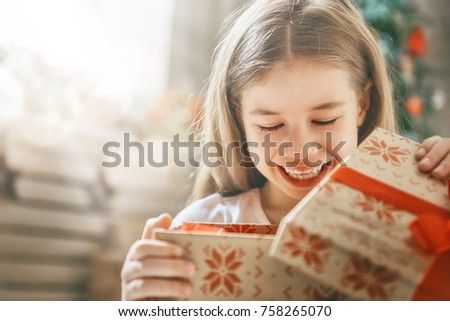 Happy holidays! Cute little child opening gift at Christmas.