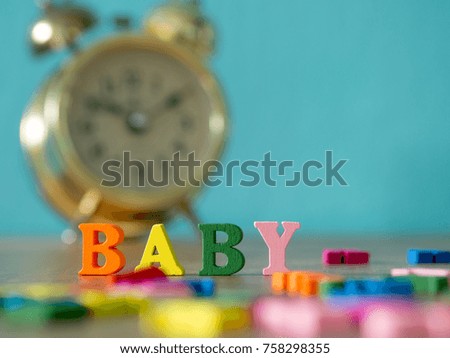 Baby. English alphabet made of wooden letter color. Alphabet baby on wooden table and vintage alarm clock and background is powder blue.