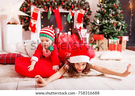 brother and sister in Christmas costumes dwarfs fun to play near the fireplace and Christmas tree