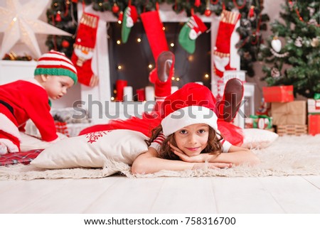 brother and sister in Christmas costumes dwarfs fun to play near the fireplace and Christmas tree