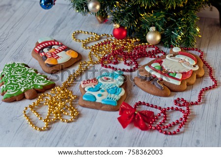 Festive composition. Honey cakes with glazed pictures of Santa, pine, penguin and snowman with numbers on  postcard laying under decorated christmas tree branch on light wooden table