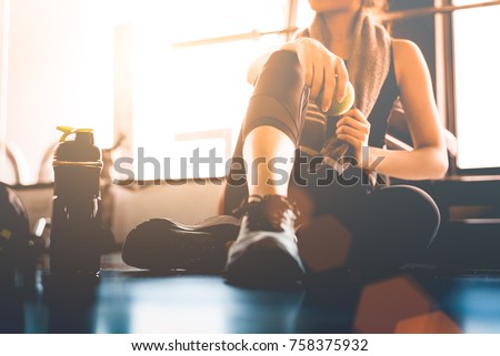 Sport woman sitting and resting after workout or exercise in fitness gym with protein shake or drinking water on floor. Relax concept. Strength training and Body build up theme. Warm and cool tone  Royalty-Free Stock Photo #758375932