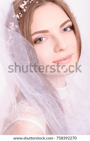 Young beautiful blond fiancee portrait with white veil on light background looking at camera smiling.
