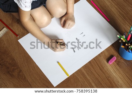 Girl draws picture with crayons on the sheet of paper on the floor
