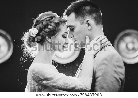 Portrait of beautiful young couple young gorgeous bride and handsome groom at rounded light background. Sweet, beloved sweathearts leaning by nose each other, embracing and touching by faces. Wedding. Royalty-Free Stock Photo #758437903