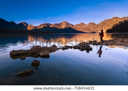 Unidentified photographer at Segara Anak Lake in early morning. Mount Rinjani is an active volcano in Lombok, Indonesia. Soft focus due to long exposure. 