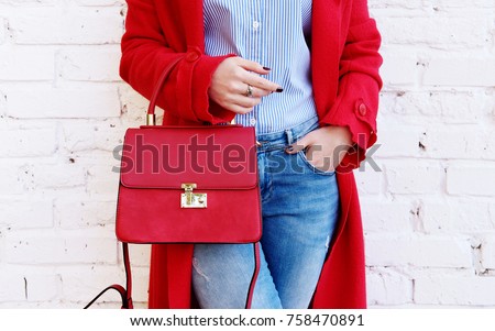 Closeup of red small bag in hand of woman. Fall spring fashion outfit red coat and trendy blue jeans Royalty-Free Stock Photo #758470891