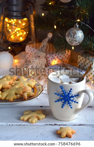 Christmas and new year holiday celebration concept background. Cup of cocoa with marshmallow, homemade chocolate cookie and peanut biscuit, lighted candles, xmas tree decoration on wooden table.
