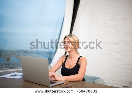 Happy woman financier working with important electronic documents on laptop computer, sitting in modern office near big window.Smiling female student keyboarding on portable net-book, learning on-line