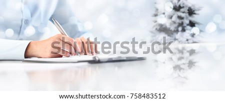 Christmas theme Woman's hands writing on sheet of paper in a clipboard with pen isolated on desk on christmas tree background