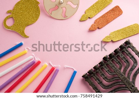 Image of jewish holiday Hanukkah with wooden dreidels (spinning top) , candles, menora (traditional Candelabra) , children's stickers glitter craft- jug of Chanukah and candles on pink background.