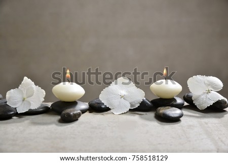 hydrangea petals with black stones and candle on gray background
