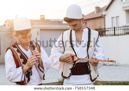 teen boys in traditional albanian costume playing music with flute and string instrument in the evening sunlight Royalty-Free Stock Photo #758557348