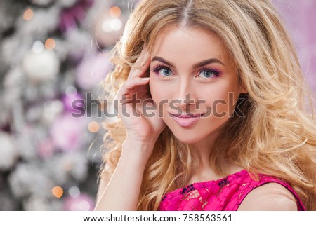 Beautiful young girl with long wavy hair in a pink dress on a background of the Christmas tree. Christmas and New Year in the picture.