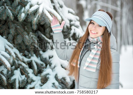 A girl dressed in warm winter clothes and a hat posing in a winter forest. Smiling girl is happy with snow and winter.