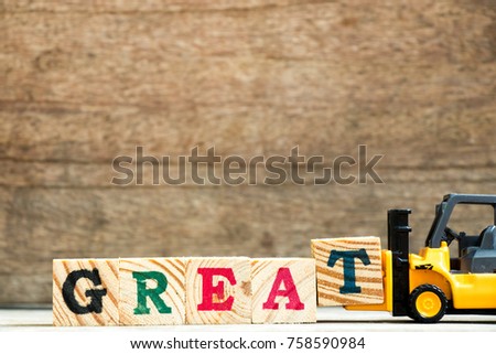 Yellow plastic toy forklift hold letter block T to complete word great on wood background