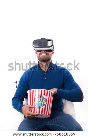 Young man smiles while watching a film on his virtual reality device, he is holding a popcorn bucket. Isolated on white background
