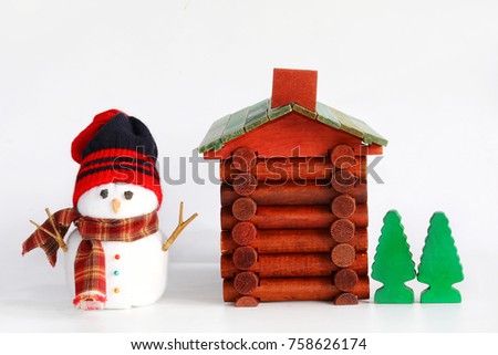 Snowman doll, log cabin with chimney, green tree toy isolated on white. Snowman wear black, red beanie knitting hat and red, brown plaid scarf. Dry sticks used for arms, coal for eyes, stone for nose