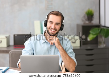 Young man using laptop and listening to music in office