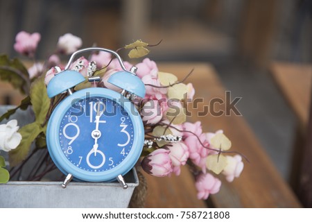 Blue clock with Artificial Flowers as a background or wallpaper.