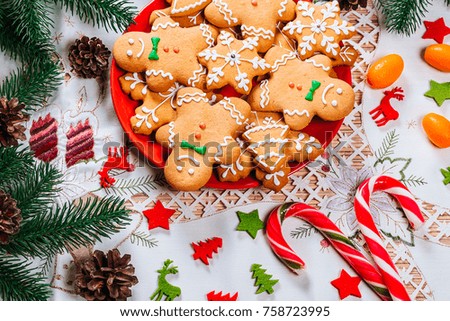 Christmas gingerbread cookies homemade on red plate with branches of Christmas tree and decor on home New Year table. Merry Christmas postcard.