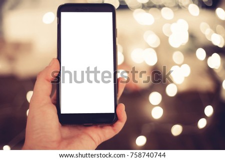 hand holding smart phone with empty screen on background of christmas lights in evening. space for text. happy holidays. black friday sale. vintage tone. merry christmas greetings