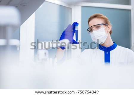 I knew it. Young beautiful  laboratorian examining liquid in test glass while wearing special mask and glasses and standing in the lab