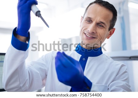 Seems clear. Attractive  glad male laboratorian conducting procedure while holding vial and smiling when standing against the blurred background