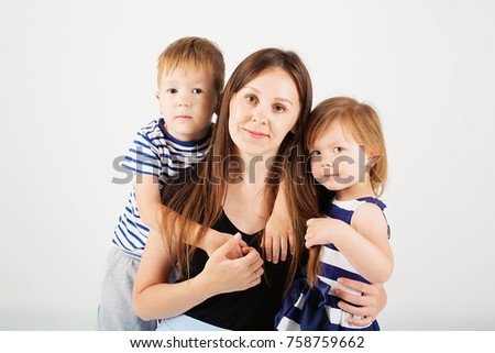 Portrait of a happy mother and her two little children - boy and girl. Happy family against a white background. Little kids kissing mother. Children with toys.