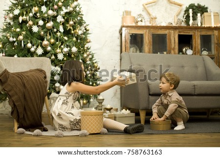 The family celebrates Christmas. Children open gifts. Brother and sister under the Christmas tree, many gifts around