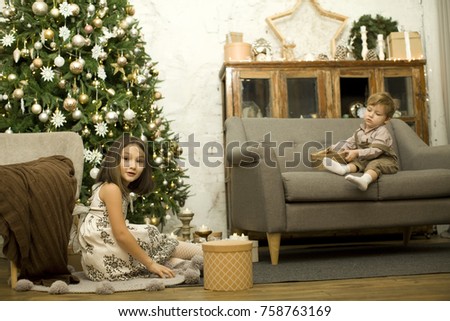 The family celebrates Christmas. Children open gifts. Brother and sister under the Christmas tree, many gifts around