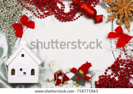 Christmas frame background with decorative elements. Ceramic house, souvenir dolls, star, snowflakes, garlands and decorations on white silk cloth. Top view with copy space.