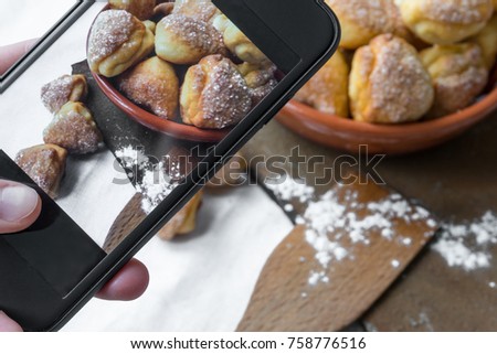 Female hand takes pictures of cottage cheese sugar cookies on mobile phone for social network pictures.