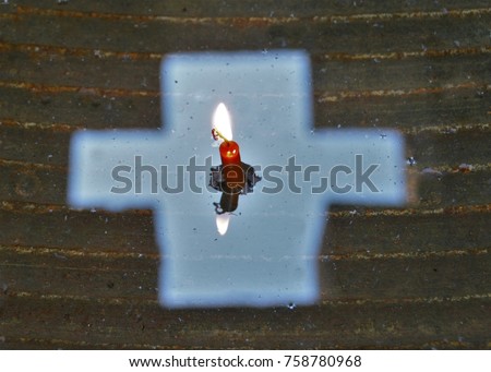candle burning in the reflection of a cross