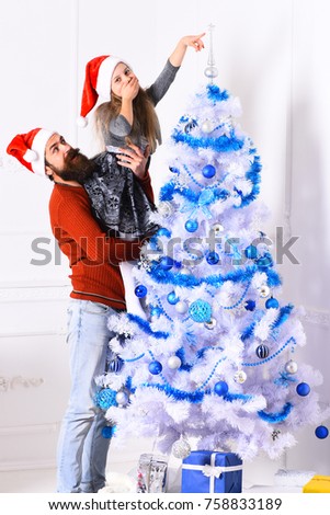 Winter holiday and party concept. Father holds little daughter putting silver top on tree. Kid and Santa decorate fir tree. Girl and bearded man with shy smiles by Christmas tree on white background
