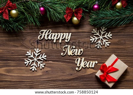 Happy New Year with two beautiful snowflakes and a gift box on the center of the wooden background with pine tree branches on the top of the screen