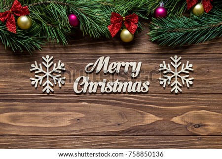 Merry Christmas on the center of the wooden background with pine tree branches on the top of the screen and two beautiful snowflakes
