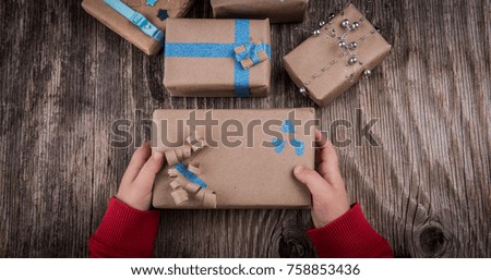 Children hands holding Christmas handmade present box on rustic wooden table