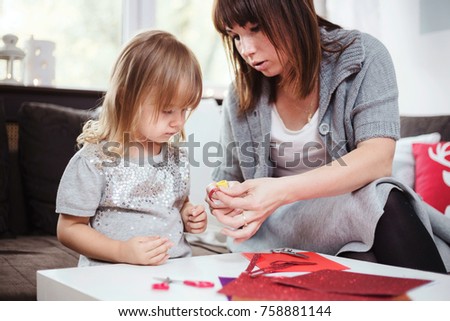 Mother and daughter making a Christmas garland with red and gold glitter paper. Lifestyle image, shallow depth of field.