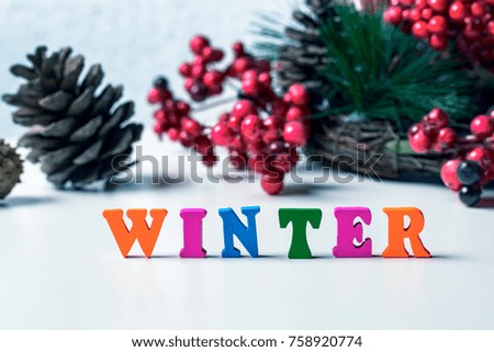 Concept of the arrival of Winter. The floor is lined with colored letters on a white table, on the background of cones and a festive wreath from the Christmas tree and viburnum