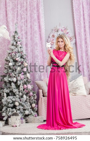 Beautiful young girl with long wavy hair in a pink dress on a background of the Christmas tree. Christmas and New Year in the picture.