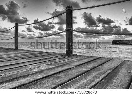 Wooden pier with ropes at the shore. Dramatic clouds in the sky. Black and white image. Wallpaper.