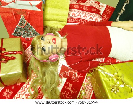 Beautiful young blonde woman in festive clothing listening to Christmas carols laying on her bed between Christmas gifts.
