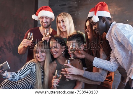 Group beautiful young people doing selfie in the new year party, best friends girls and boys together having fun, posing emotional lifestyle people. Hats santas and champagne glasses in their hands.