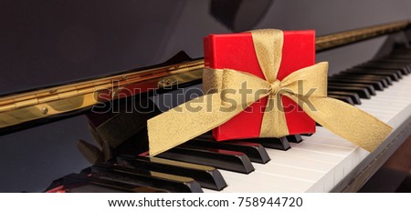Red gift box with golden bow on classical piano keyboard