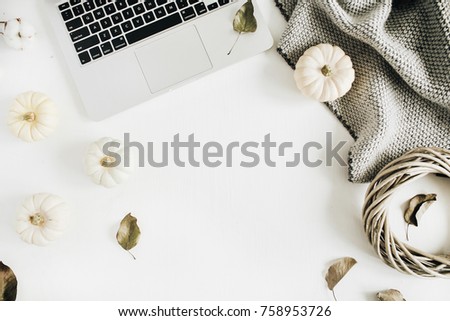 Flat lay home office desk. Workspace with laptop, white pumpkins, cotton branches, grey plaid and wreath frame. Top view autumn or winter composition.