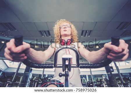 Thin blond man with glasses and red headphones training on a stationary bike